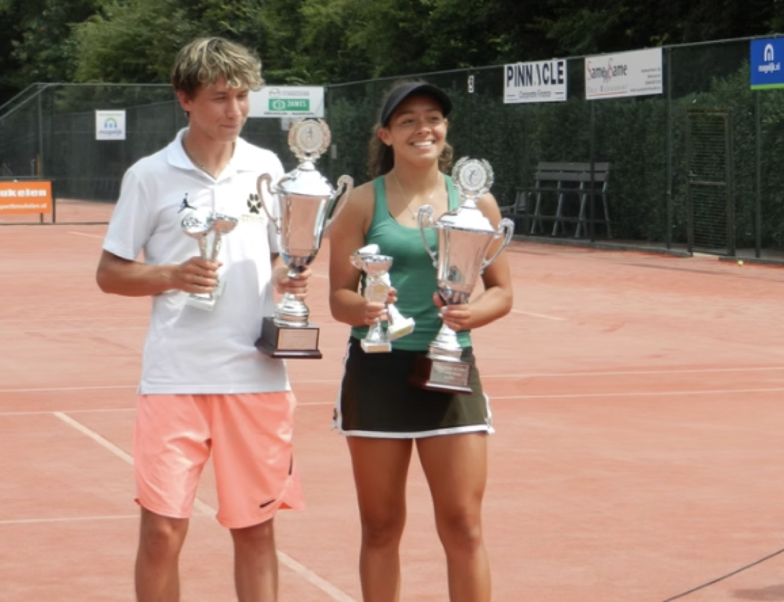 Two players holding their tournament trophies on a red clay court